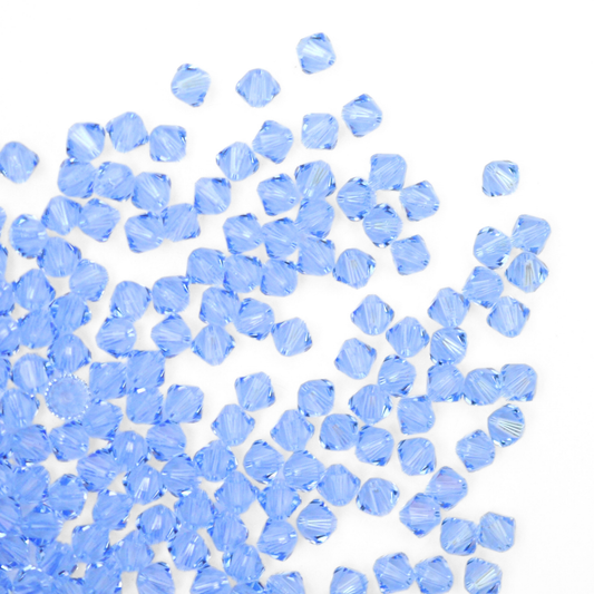 Austrian crystal 5328 bicone beads in the color Light Sapphire spilling out onto a white background. 