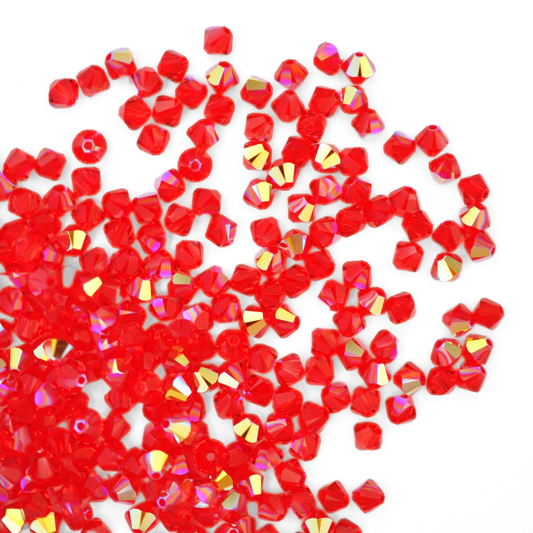Austrian crystal 5328 bicone beads in the color Light Siam AB spilling out onto a white background. 