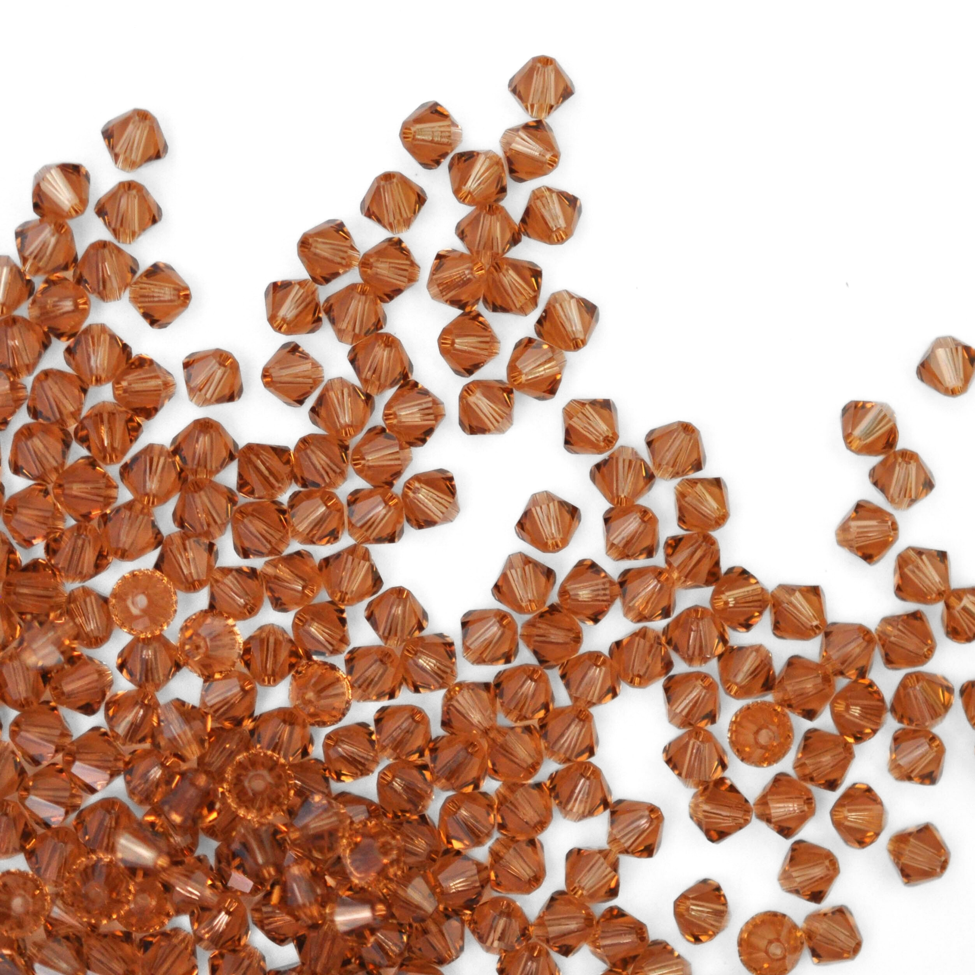 Austrian crystal 5328 bicone beads in the color Light Smoked Topaz spilling out onto a white background. 