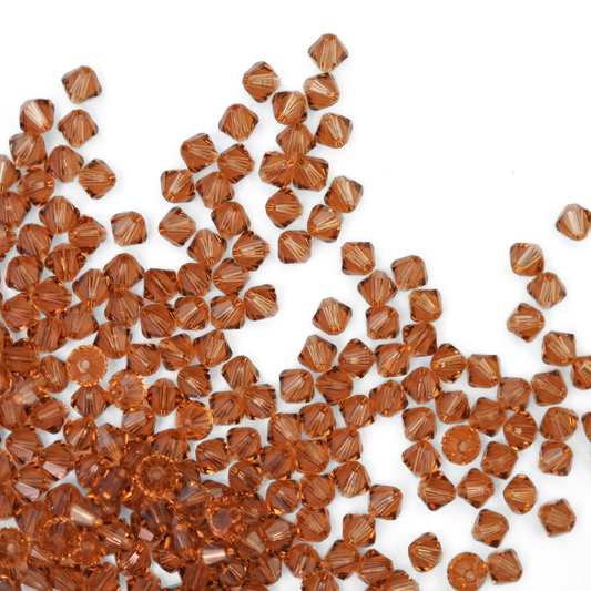 Austrian crystal 5328 bicone beads in the color Light Smoked Topaz spilling out onto a white background. 