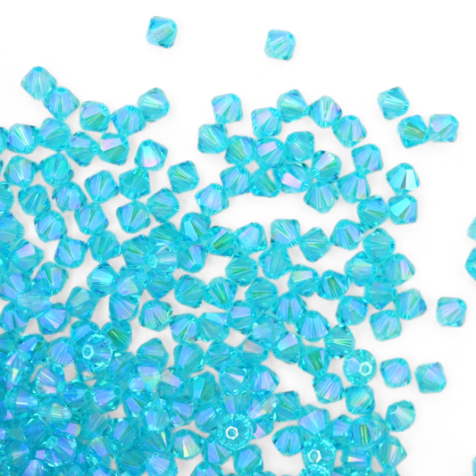 Austrian crystal 5328 bicone beads in the color Light Turquoise Shimmer 2X spilling out onto a white background. 