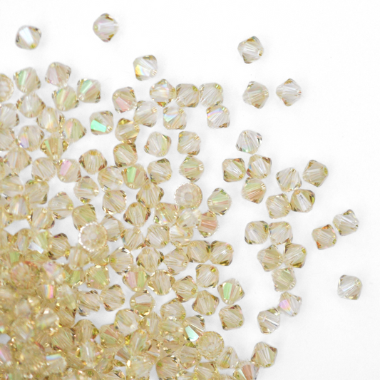 Austrian crystal 5328 bicone beads in the color Luminous Green spilling out onto a white background. 
