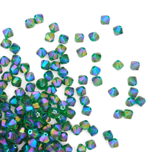 Austrian crystal 5328 bicone beads in the color Majestic Green Shimmer 2X spilling out onto a white background. 