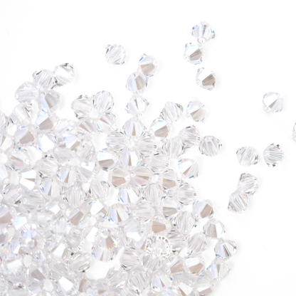 Austrian crystal 5328 bicone beads in the color Moonlight spilling out onto a white background. 