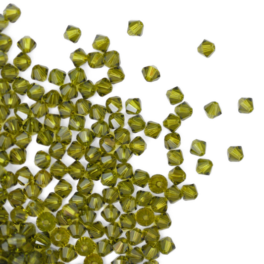 Austrian crystal 5328 bicone beads in the color Olivine spilling out onto a white background. 