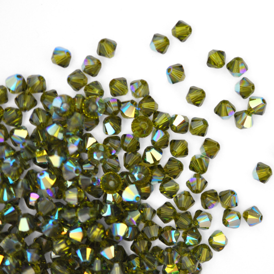 Austrian crystal 5328 bicone beads in the color Olivine spilling out onto a white background. 