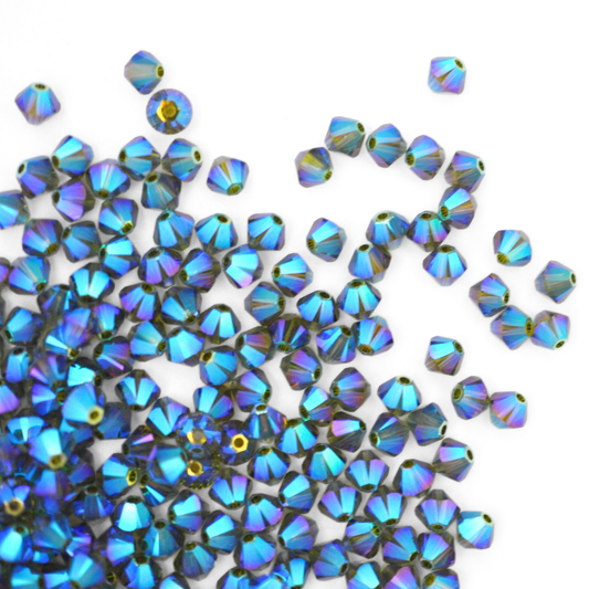 Austrian crystal 5328 bicone beads in the color Olivine AB 2X spilling out onto a white background. 