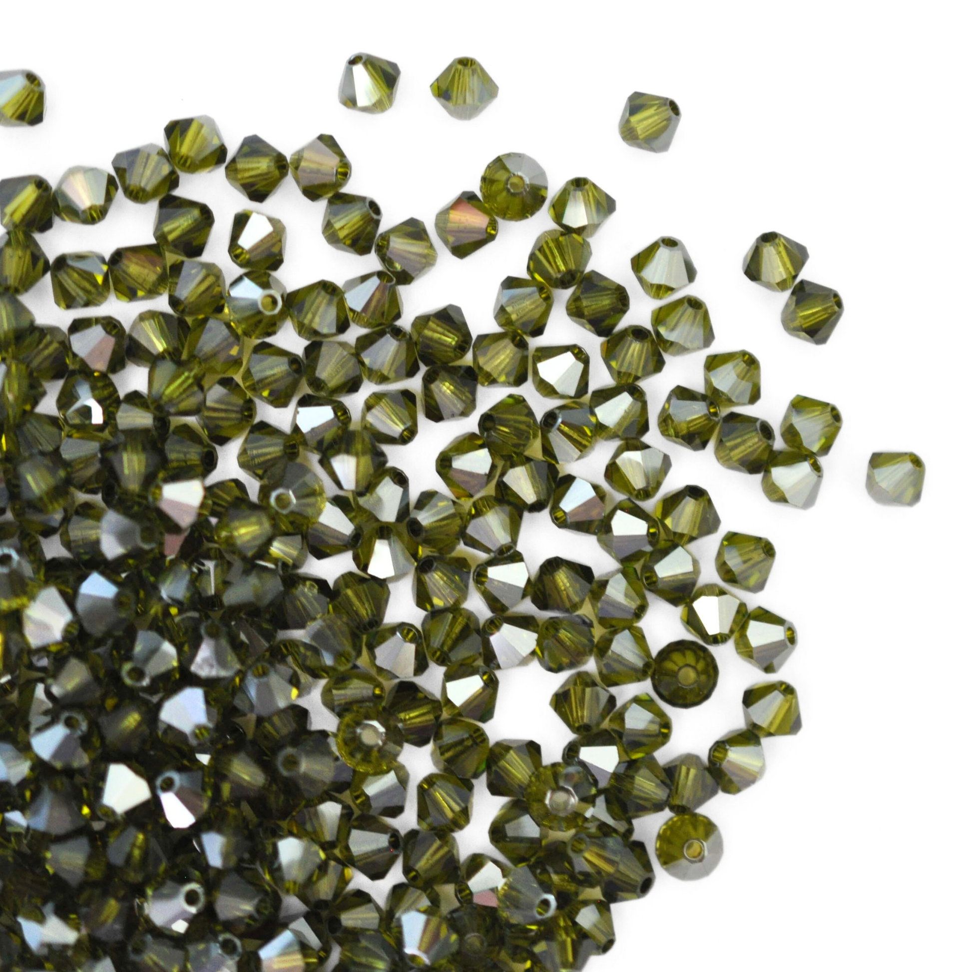 Austrian crystal 5328 bicone beads in the color Olivine Satin spilling out onto a white background. 