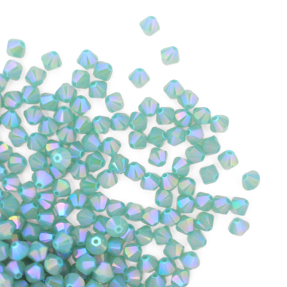 Austrian crystal 5328 bicone beads in the color Pacific Opal Shimmer 2X spilling out onto a white background. 