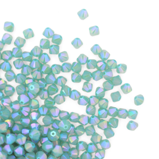 Austrian crystal 5328 bicone beads in the color Pacific Opal Shimmer 2X spilling out onto a white background. 