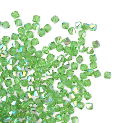 Austrian crystal 5328 bicone beads in the color Peridot AB spilling out onto a white background. 
