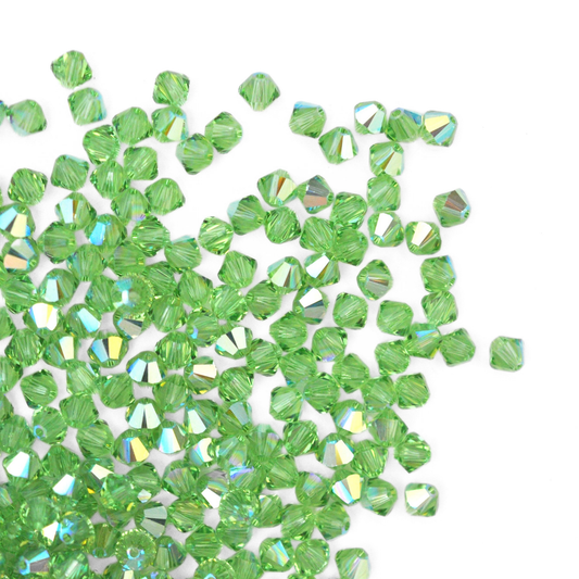 Austrian crystal 5328 bicone beads in the color Peridot AB spilling out onto a white background. 