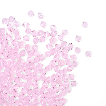 Austrian crystal 5328 bicone beads in the color Rosaline spilling out onto a white background. 