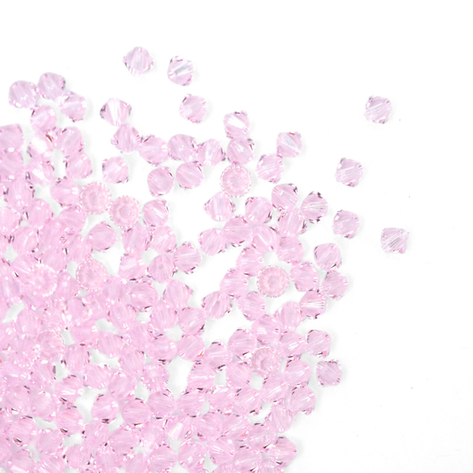 Austrian crystal 5328 bicone beads in the color Rosaline spilling out onto a white background. 