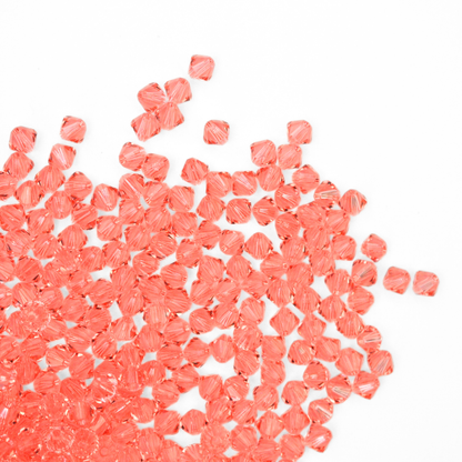 Austrian crystal 5328 bicone beads in the color Rose Peach spilling out onto a white background. 