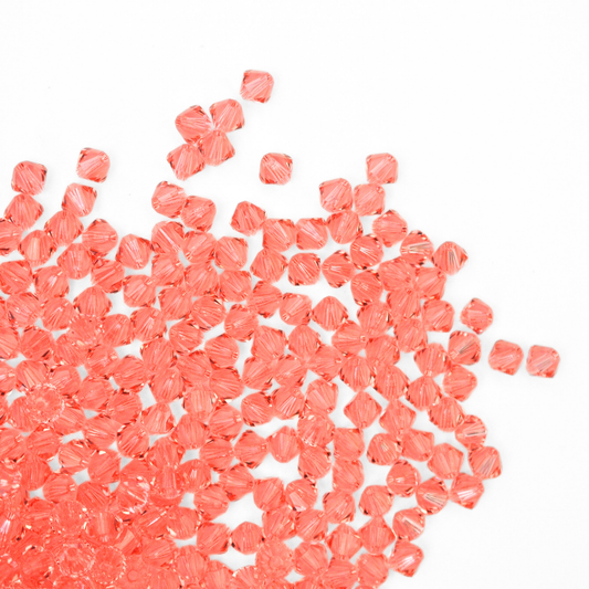 Austrian crystal 5328 bicone beads in the color Rose Peach spilling out onto a white background. 