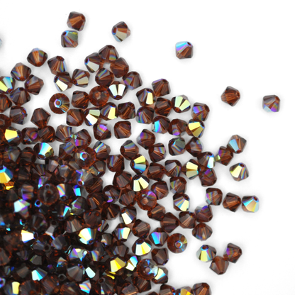 Austrian crystal 5328 bicone beads in the color Smoked Topaz AB spilling out onto a white background. 