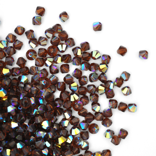 Austrian crystal 5328 bicone beads in the color Smoked Topaz AB spilling out onto a white background. 