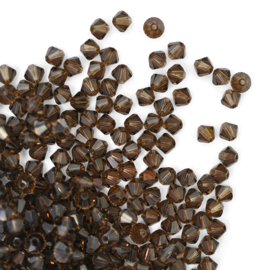 Austrian crystal 5328 bicone beads in the color Smoky Quartz spilling out onto a white background. 