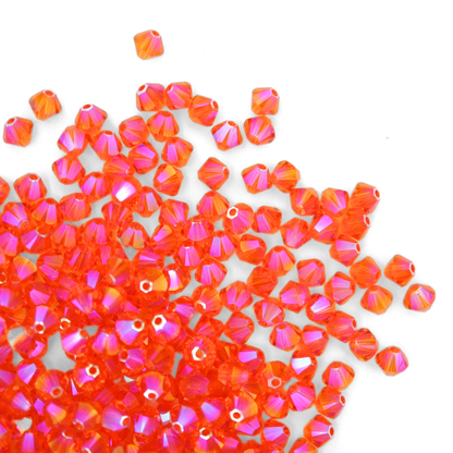 Austrian crystal 5328 bicone beads in the color Tangerine Shimmer 2X spilling out onto a white background. 