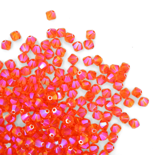 Austrian crystal 5328 bicone beads in the color Tangerine Shimmer 2X spilling out onto a white background. 