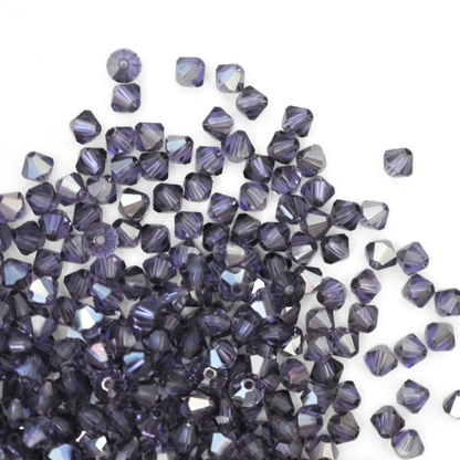 Austrian crystal 5328 bicone beads in the color Tanzanite Satin spilling out onto a white background. 