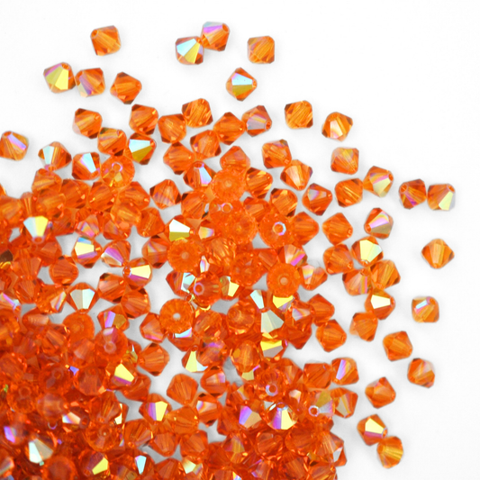 Austrian crystal 5328 bicone beads in the color Topaz AB spilling out onto a white background. 