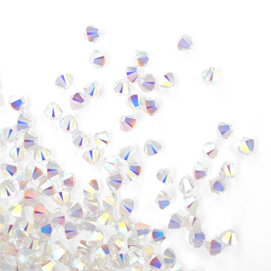 Austrian crystal 5328 bicone beads in the color Crystal Transmission 2X spilling out onto a white background. 