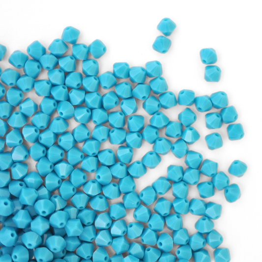 Austrian crystal 5328 bicone beads in the color Turquoise spilling out onto a white background. 