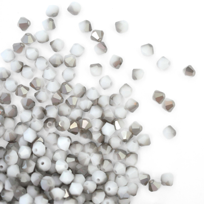 Austrian crystal 5328 bicone beads in the color White Alabaster Satin spilling out onto a white background. 