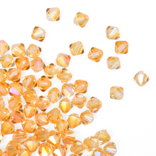 Austrian crystal 5328 bicone beads in the color Amber spilling out onto a white background. 
