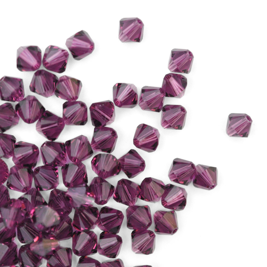 Austrian crystal 5328 bicone beads in the color Amethyst spilling out onto a white background. 