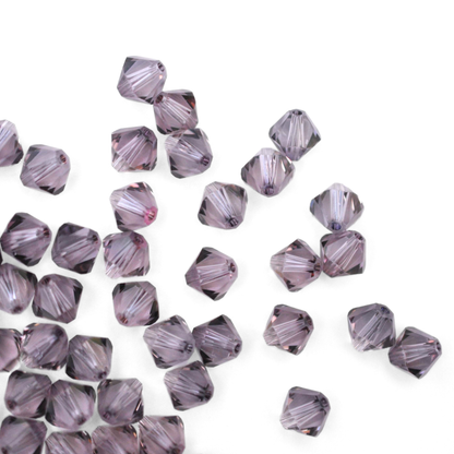 Austrian crystal 5328 bicone beads in the color Antique Pink spilling out onto a white background. 