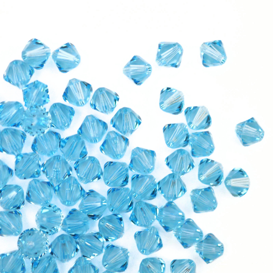 Austrian crystal 5328 bicone beads in the color Aquamarine spilling out onto a white background. 