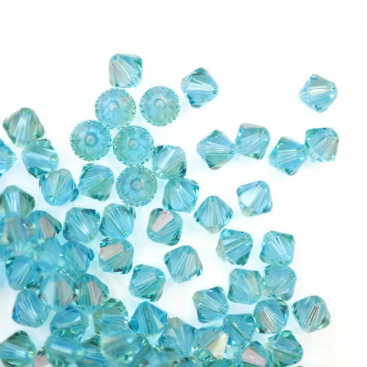 Austrian crystal 5328 bicone beads in the color Aquamarine Champagne spilling out onto a white background. 
