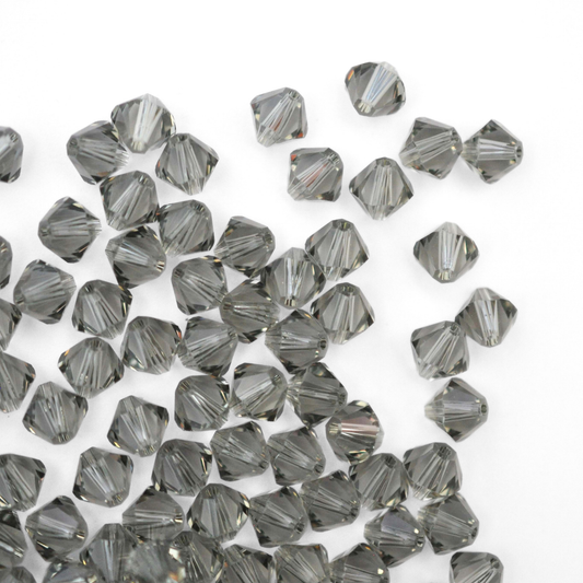 Austrian crystal 5328 bicone beads in the color Black Diamond spilling out onto a white background. 