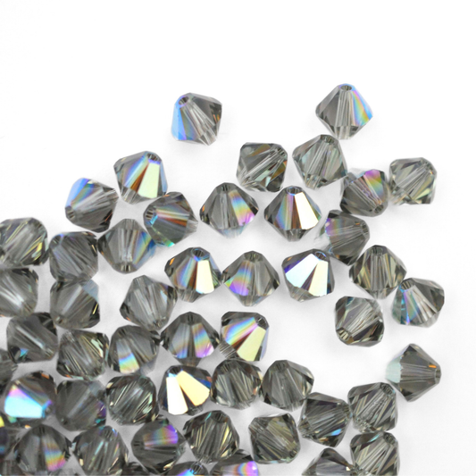 Austrian crystal 5328 bicone beads in the color Black Diamond AB spilling out onto a white background. 