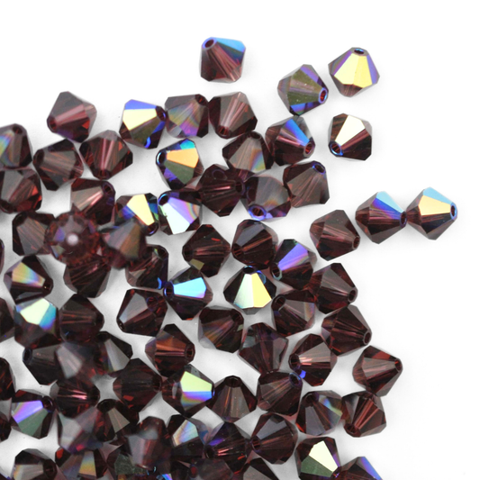 Austrian crystal 5328 bicone beads in the color Burgundy AB spilling out onto a white background. 