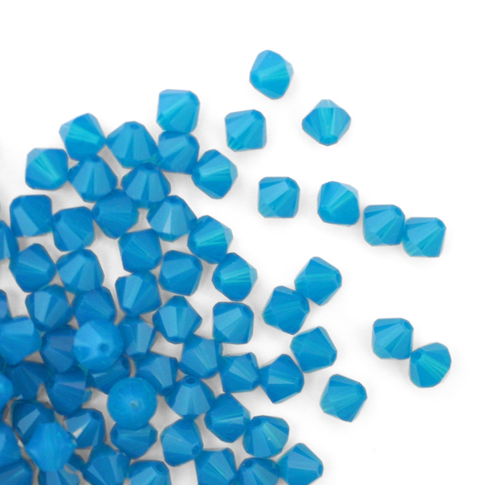 Austrian crystal 5328 bicone beads in the color Caribbean Blue Opal spilling out onto a white background. 