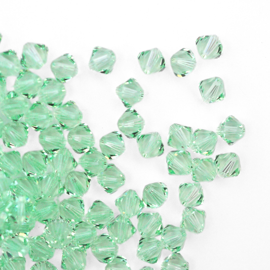 Austrian crystal 5328 bicone beads in the color Chrysolite spilling out onto a white background. 