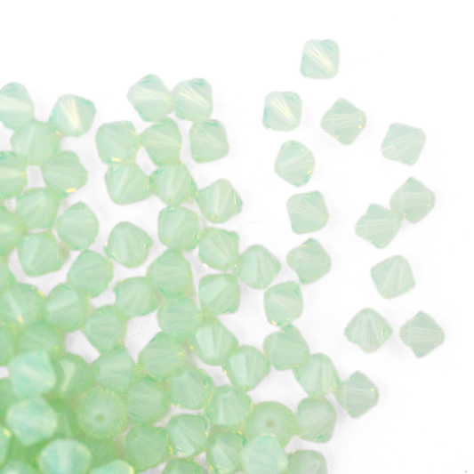 Austrian crystal 5328 bicone beads in the color Chrysolite Opal spilling out onto a white background. 