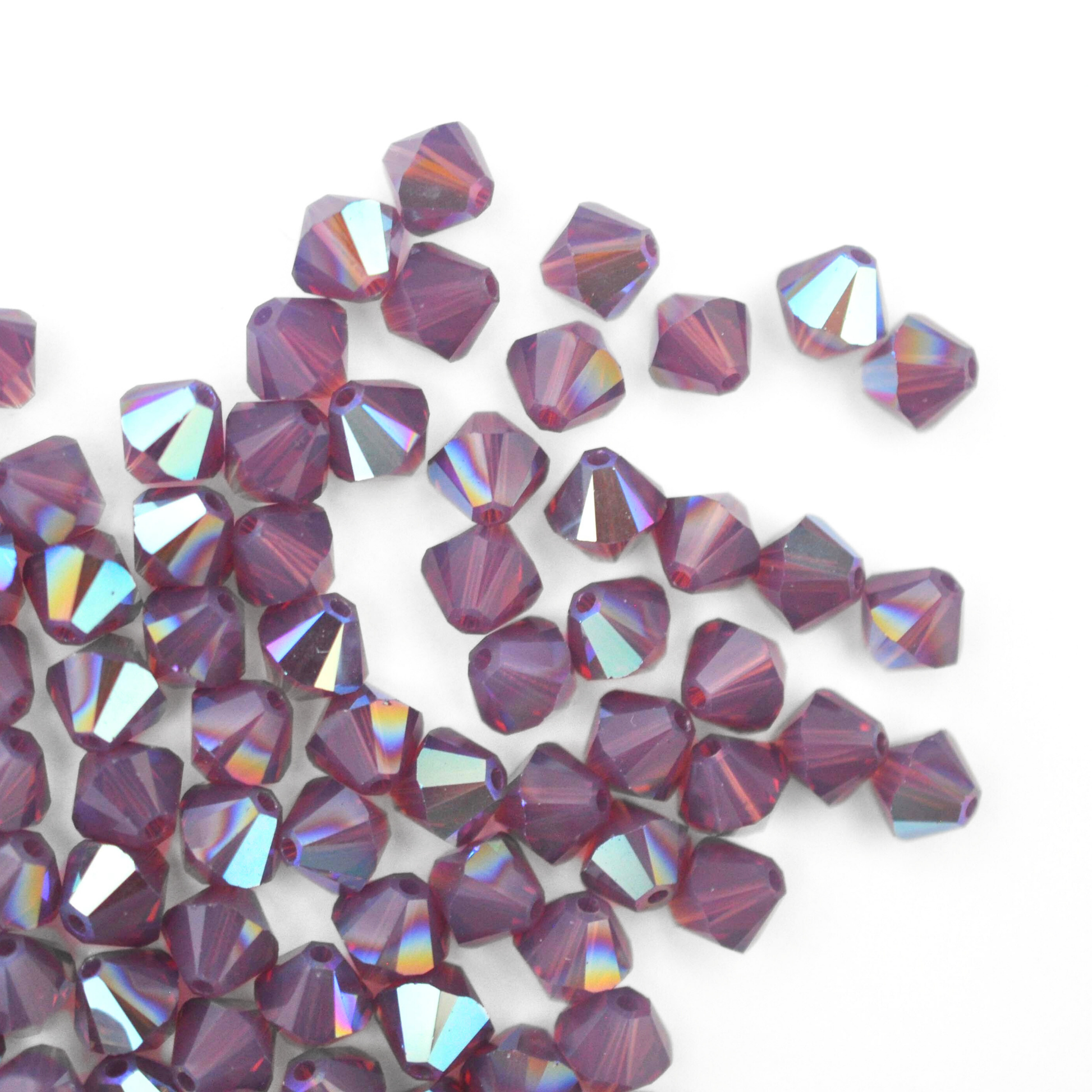 Austrian crystal 5328 bicone beads in the color Cyclamen Opal AB spilling out onto a white background. 