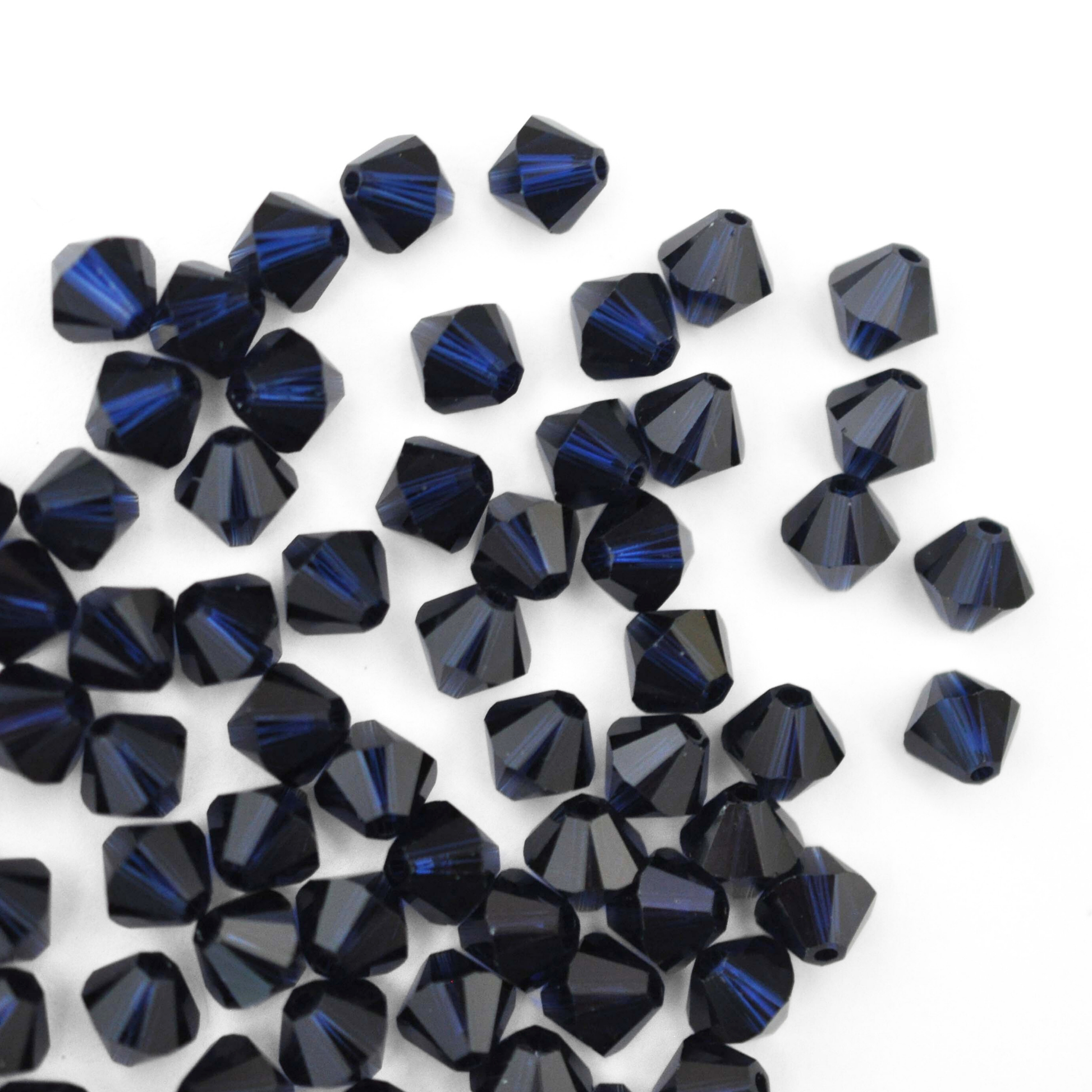 Austrian crystal 5328 bicone beads in the color Dark Indigo spilling out onto a white background. 