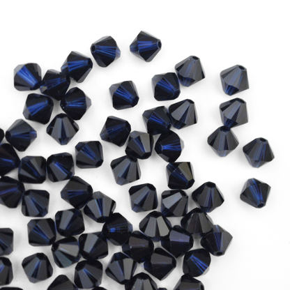 Austrian crystal 5328 bicone beads in the color Dark Indigo spilling out onto a white background. 
