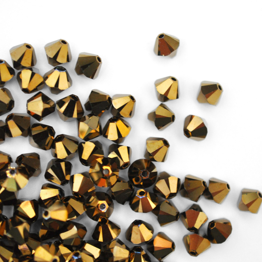 Austrian crystal 5328 bicone beads in the color Dorado spilling out onto a white background. 