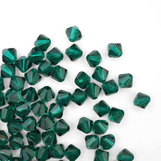 Austrian crystal 5328 bicone beads in the color Emerald spilling out onto a white background. 