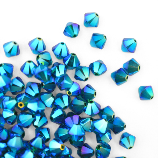 Austrian crystal 5328 bicone beads in the color Emerald AB 2X spilling out onto a white background. 