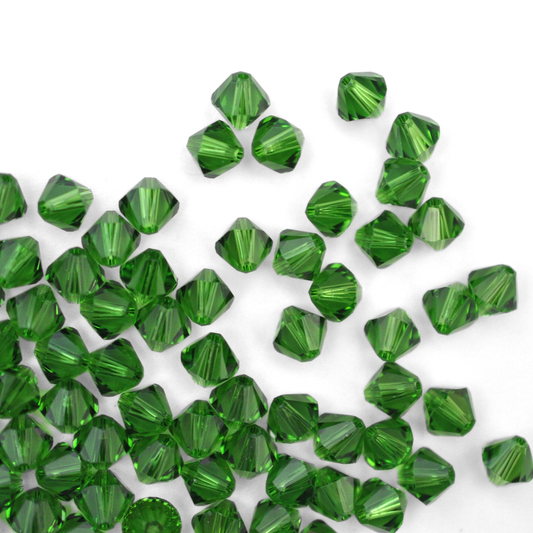 Austrian crystal 5328 bicone beads in the color Fern Green spilling out onto a white background. 