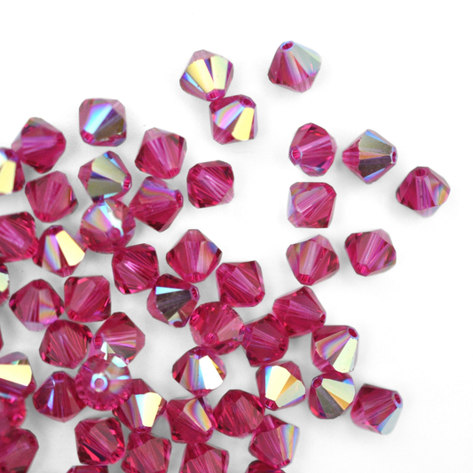 Austrian crystal 5328 bicone beads in the color Fuchsia AB spilling out onto a white background. 