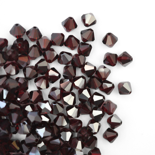 Austrian crystal 5328 bicone beads in the color Garnet Satin spilling out onto a white background. 